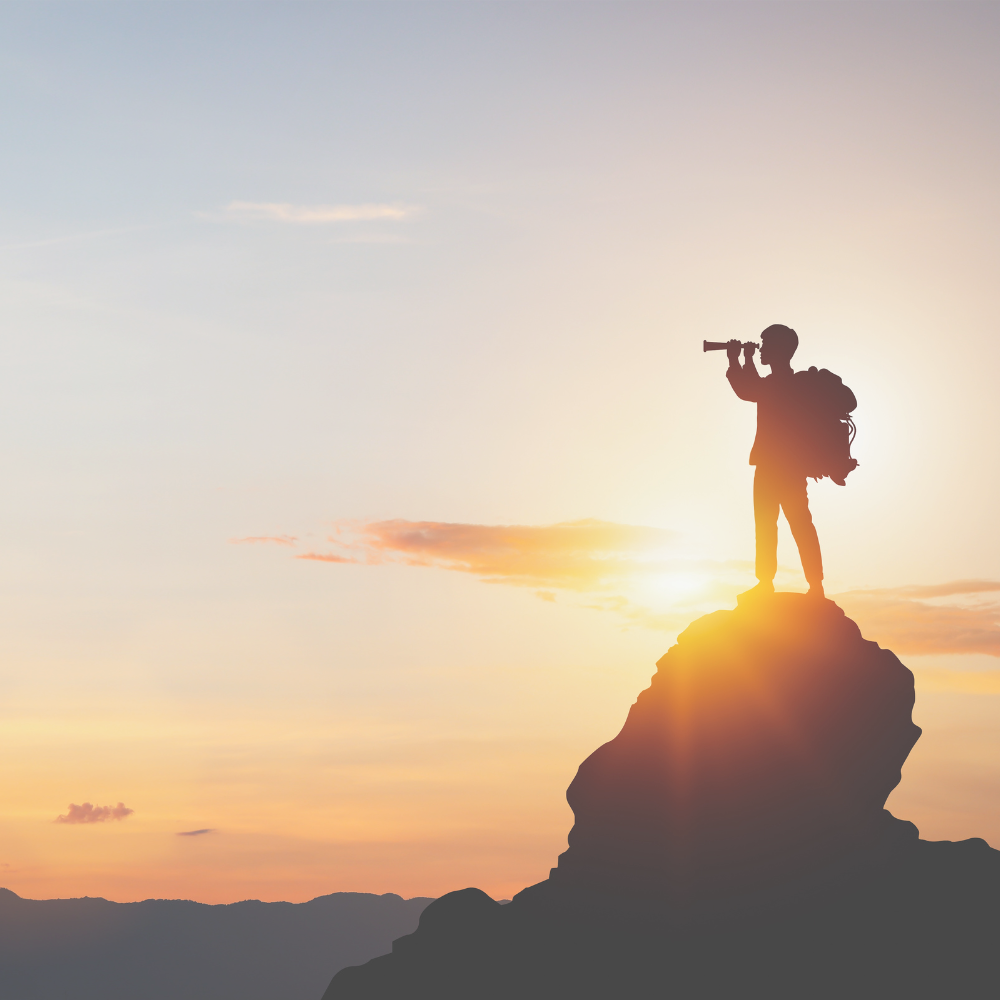 Eine Person steht auf einem Berg und schaut mit dem Fernglas in die Ferne.