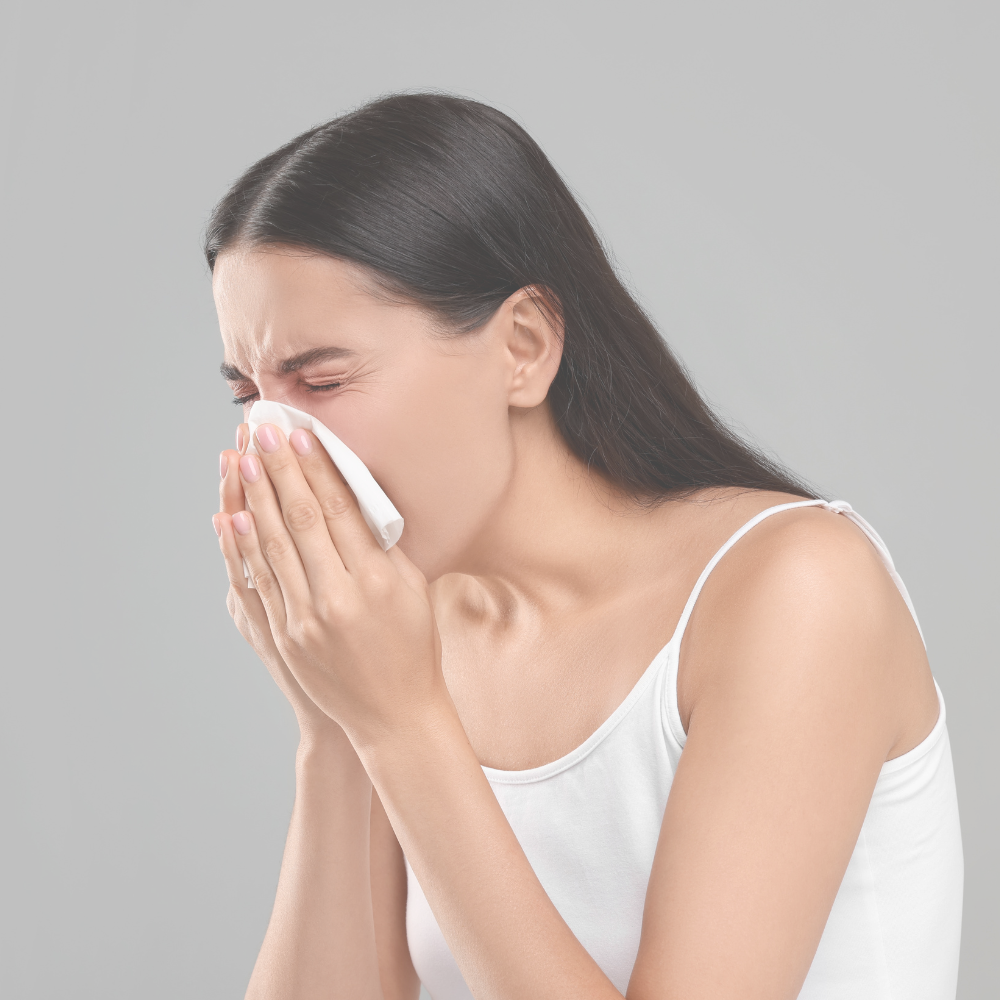 Eine Frau hält ein Taschentuch vor ihr Gesicht und niest hinein.